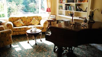 Una sala de estar con un sofá floral, una mesa de centro de madera, un piano de cola y una estantería llena de libros y objetos decorativos.