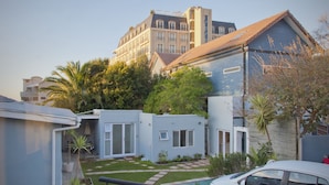 Un barrio residencial con una casa azul, un coche blanco y un edificio grande al fondo.