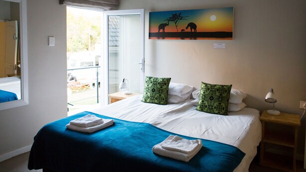 Habitación de hotel con cama, mesita de noche, ventana y un cuadro de elefantes en la pared.