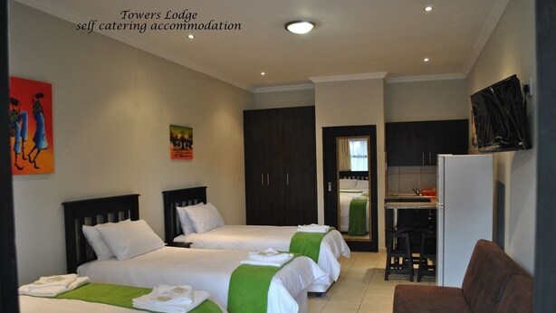 Habitación de hotel con tres camas, kitchenette, televisor y obras de arte en las paredes.