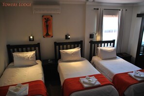 A hotel room with three single beds, each with white bedding and red throw blankets. There are wall-mounted nightstands with lamps, and a painting on the wall. - Towers Lodge (Germiston)