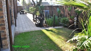 Un jardín con sendero adoquinado, bancos de piedra y diversas plantas.