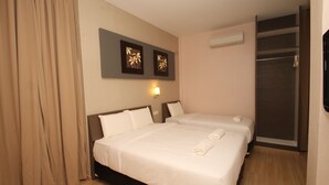 Une chambre d’hôtel avec deux lits, des rideaux beiges, un climatiseur fixé au mur et deux tableaux encadrés.