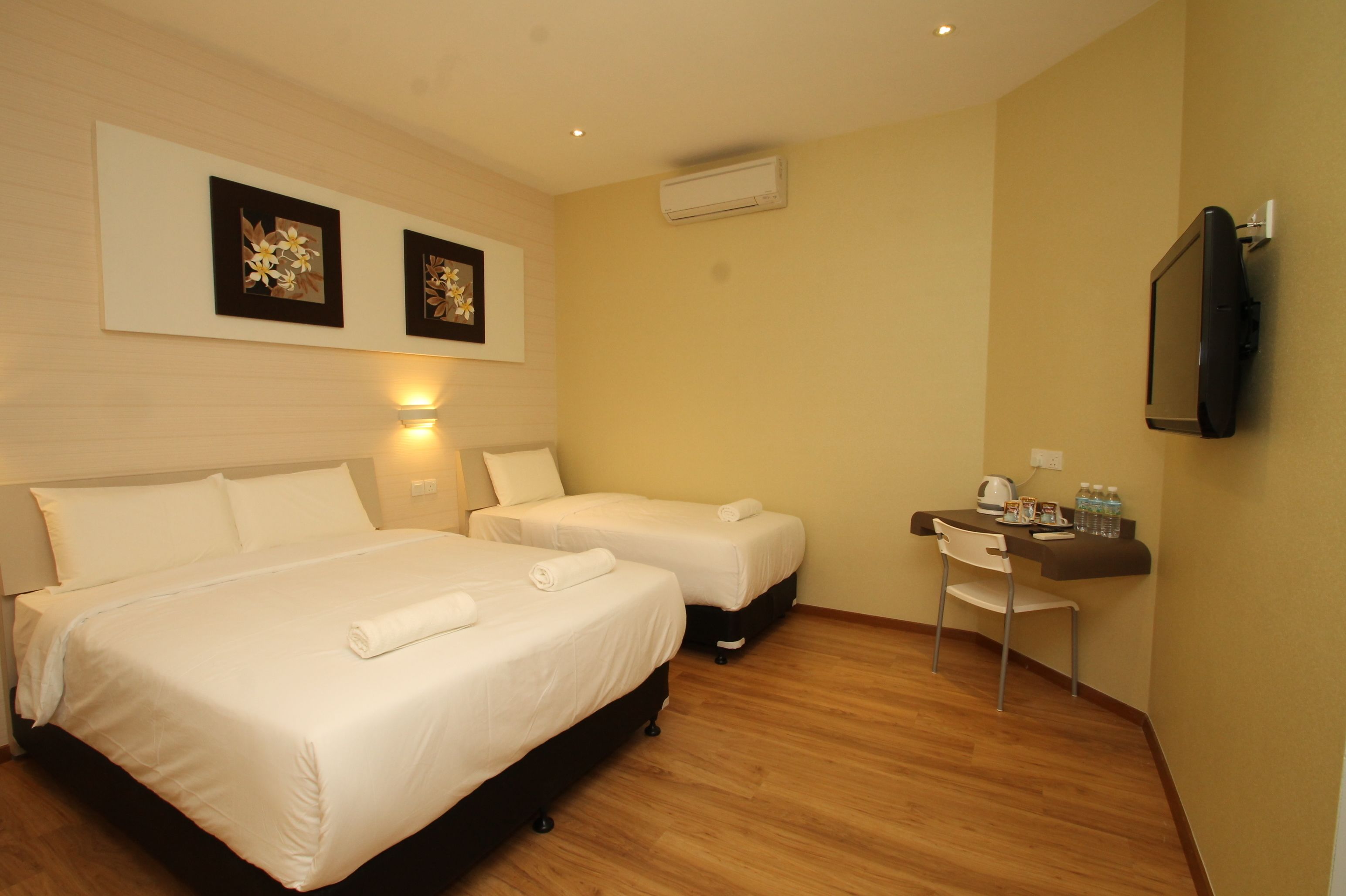 A hotel room with two beds, a desk with a chair, a flat-screen TV, and artwork on the wall.