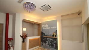 Un hall d’hôtel avec un comptoir d’accueil en bois, une photographie accrochée au mur et un lustre.