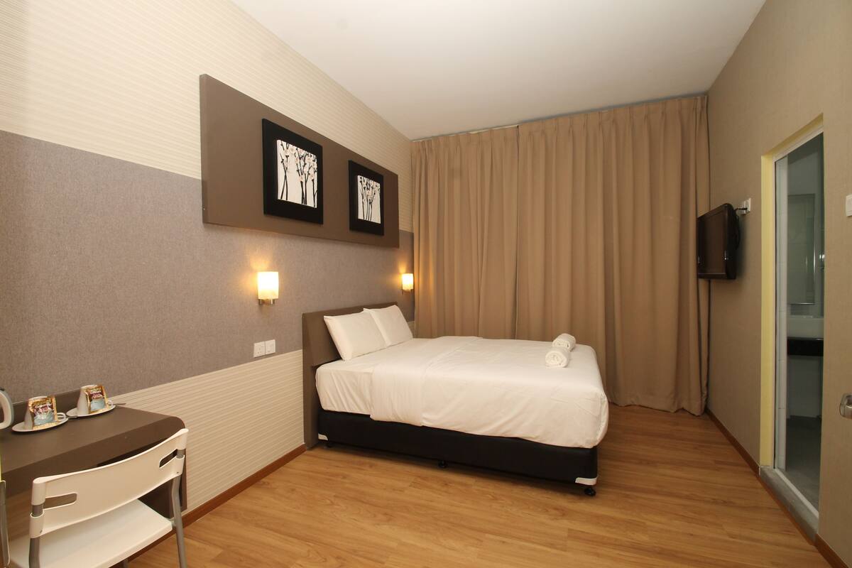 Une chambre d’hôtel comprenant un lit, un bureau avec une chaise, un téléviseur et deux cadres photos fixés au mur.
