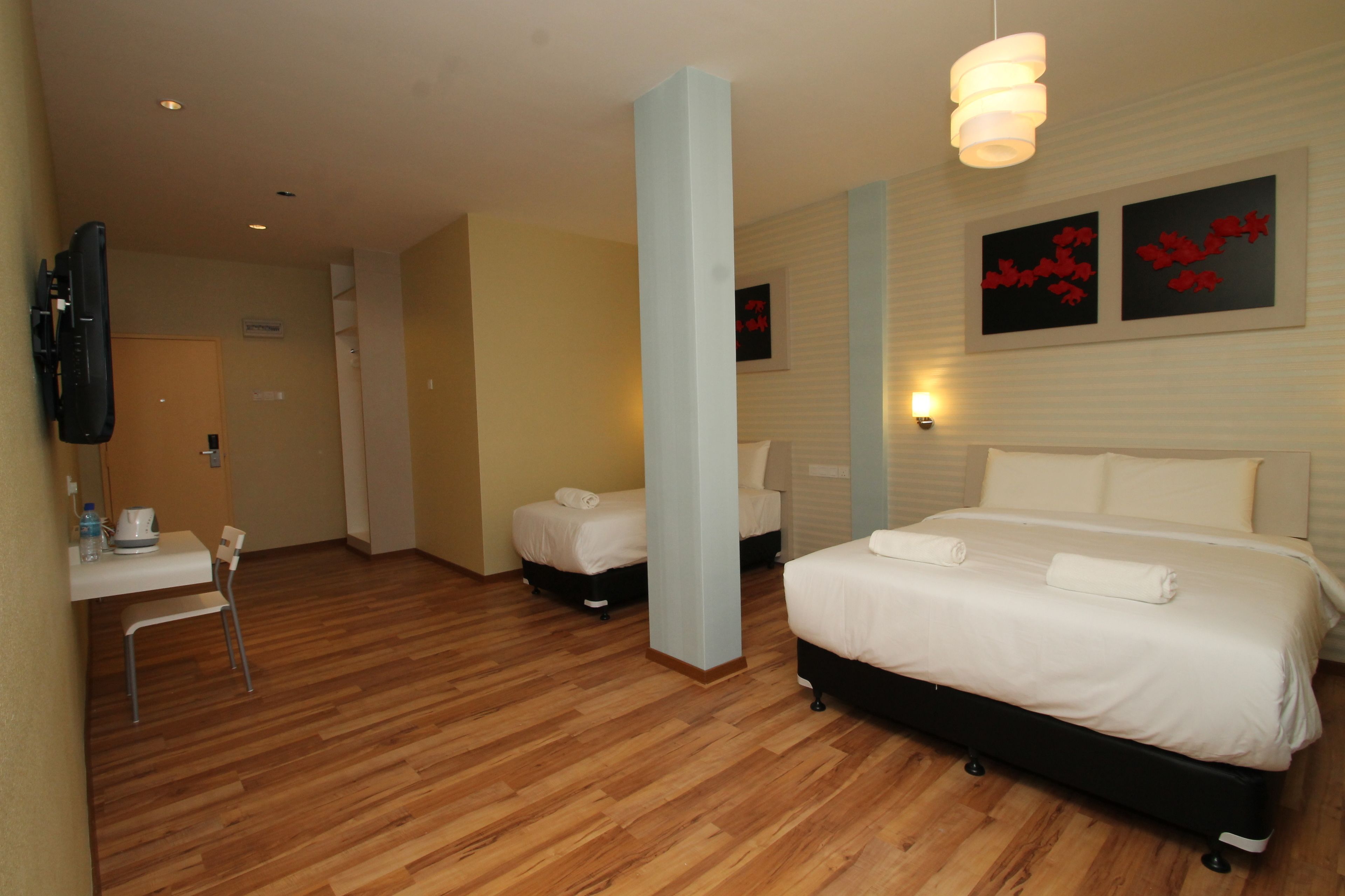 Una habitación de hotel con piso de madera, una cama con ropa de cama blanca, un escritorio con silla y un televisor montado en la pared.