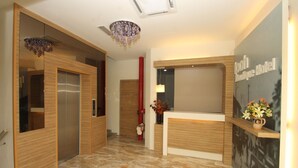 Un espace d’accueil d’hôtel au design moderne, comprenant un comptoir d’accueil, un lustre et un panneau mural.
