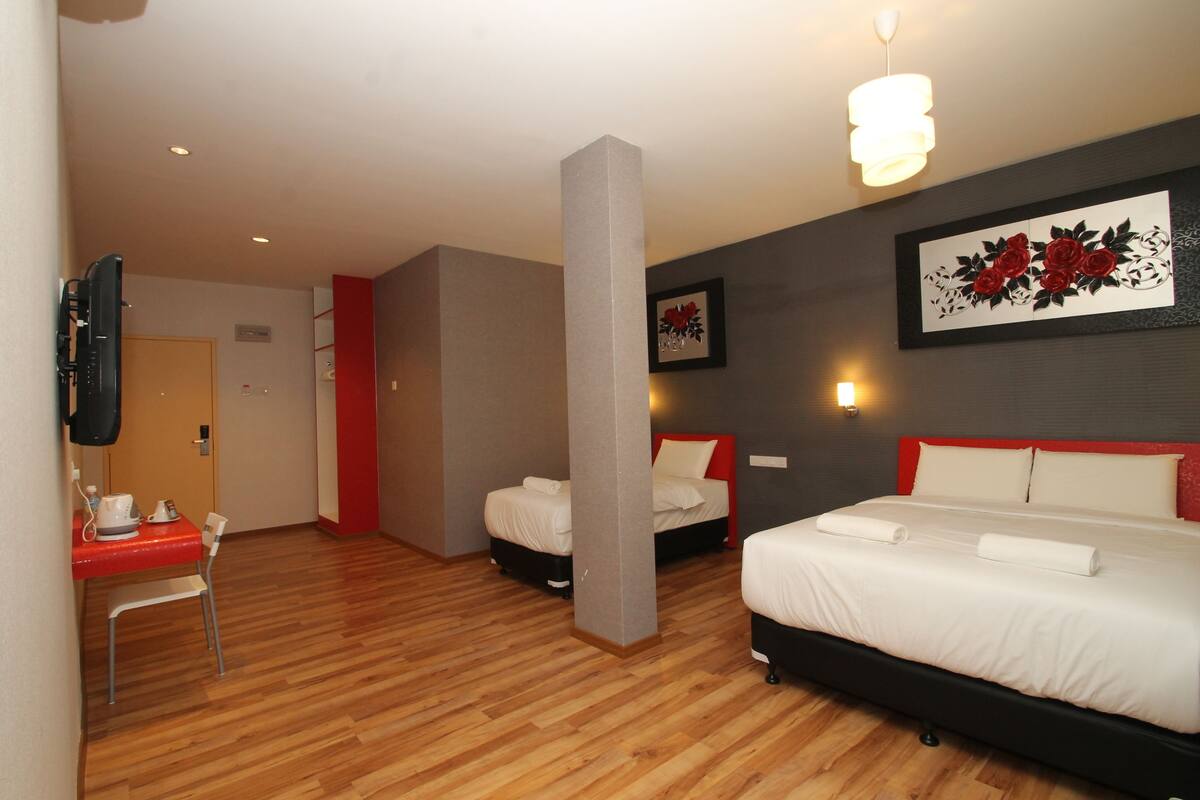 Une chambre d’hôtel avec un plancher en bois, deux lits avec une literie blanche et rouge, une chaise rouge, un téléviseur à écran plat fixé au mur et une œuvre d’art florale encadrée au-dessus des lits.