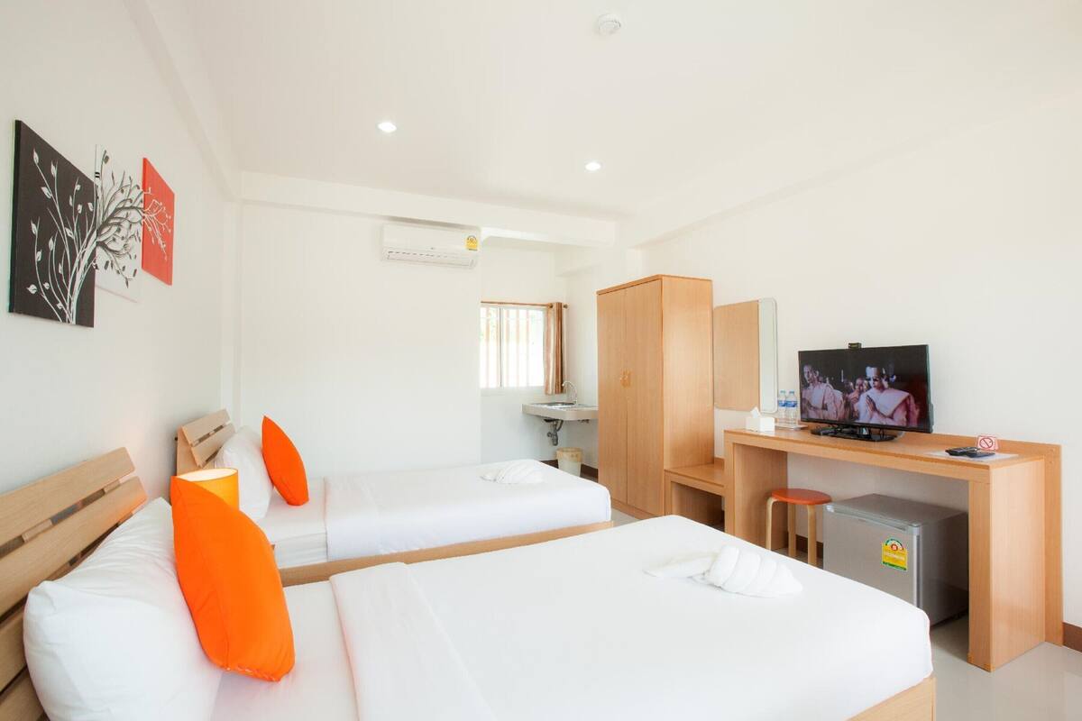 A hotel room with two beds, a desk with a television, a small refrigerator, and a window with curtains.
