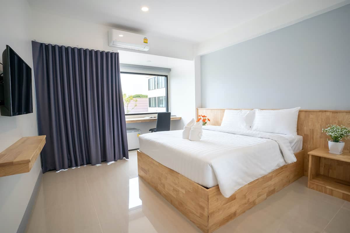 A modern hotel room with a wooden bed, a desk, a chair, a TV, and a window with curtains.
