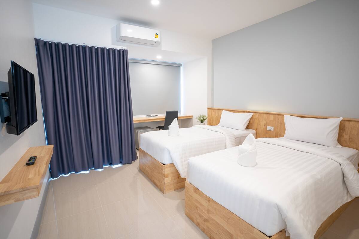 A hotel room with two beds, a desk, a TV, and a curtain.