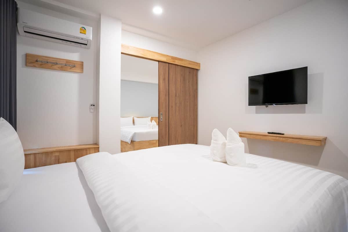 A hotel room with a bed, a TV mounted on the wall, an air conditioning unit, and a wooden shelf.