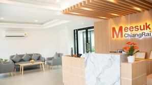 A reception area with a marble counter, a grey sofa, a wooden reception desk, and a potted plant. - Meesuk ChiangRai Hotel, SHA Certified (Chiang Rai)
