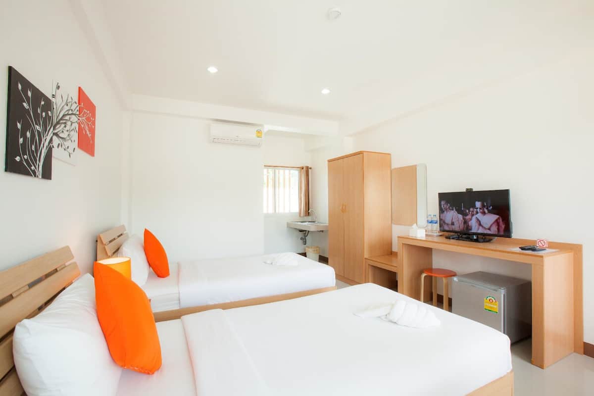 A hotel room with two beds, a desk with a television, a small refrigerator, and a window with curtains.