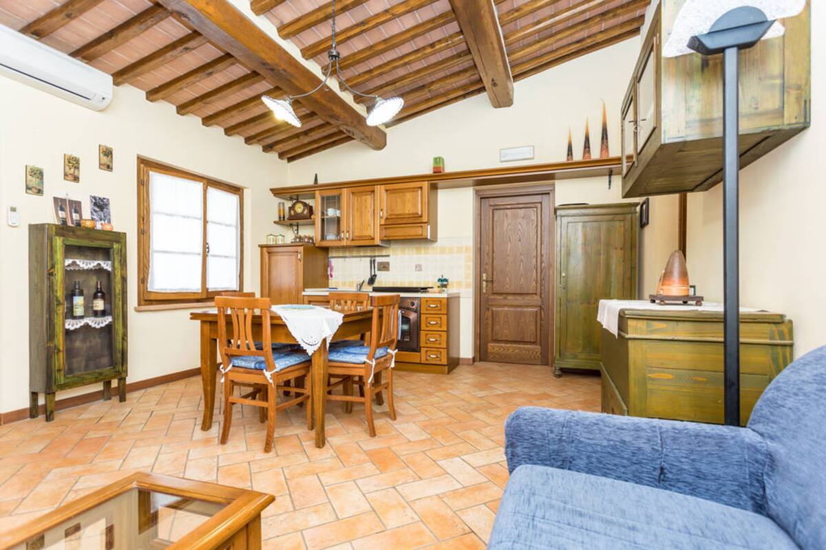 Een ruime keuken met houten kastjes, een eettafel met stoelen, en een blauwe bank in de woonkamer.