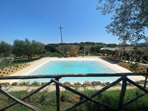 Ein rechteckiger Pool mit Holzzaun im Vordergrund, umgeben von Grünpflanzen und einem kleinen Gebäude im Hintergrund.