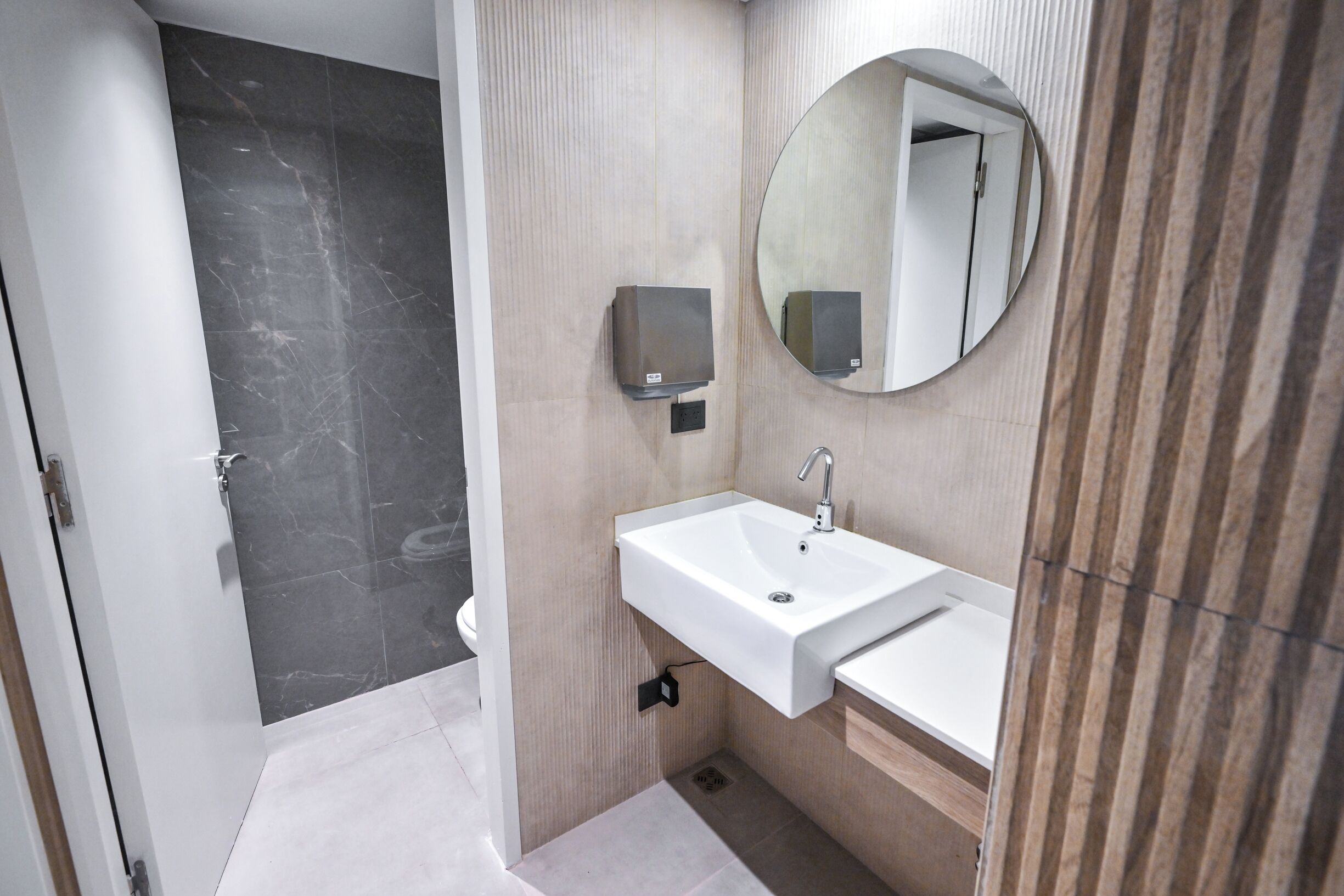 Une salle de bain moderne avec un sol en marbre, un lavabo blanc surmonté d’un miroir et des toilettes.