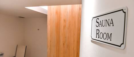 A room labeled "SAUNA ROOM" with a wooden partition and a chair.