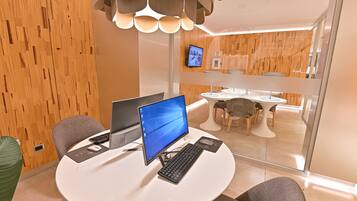 Een moderne kantoorruimte met een ronde tafel, twee computers en een televisie aan de muur.