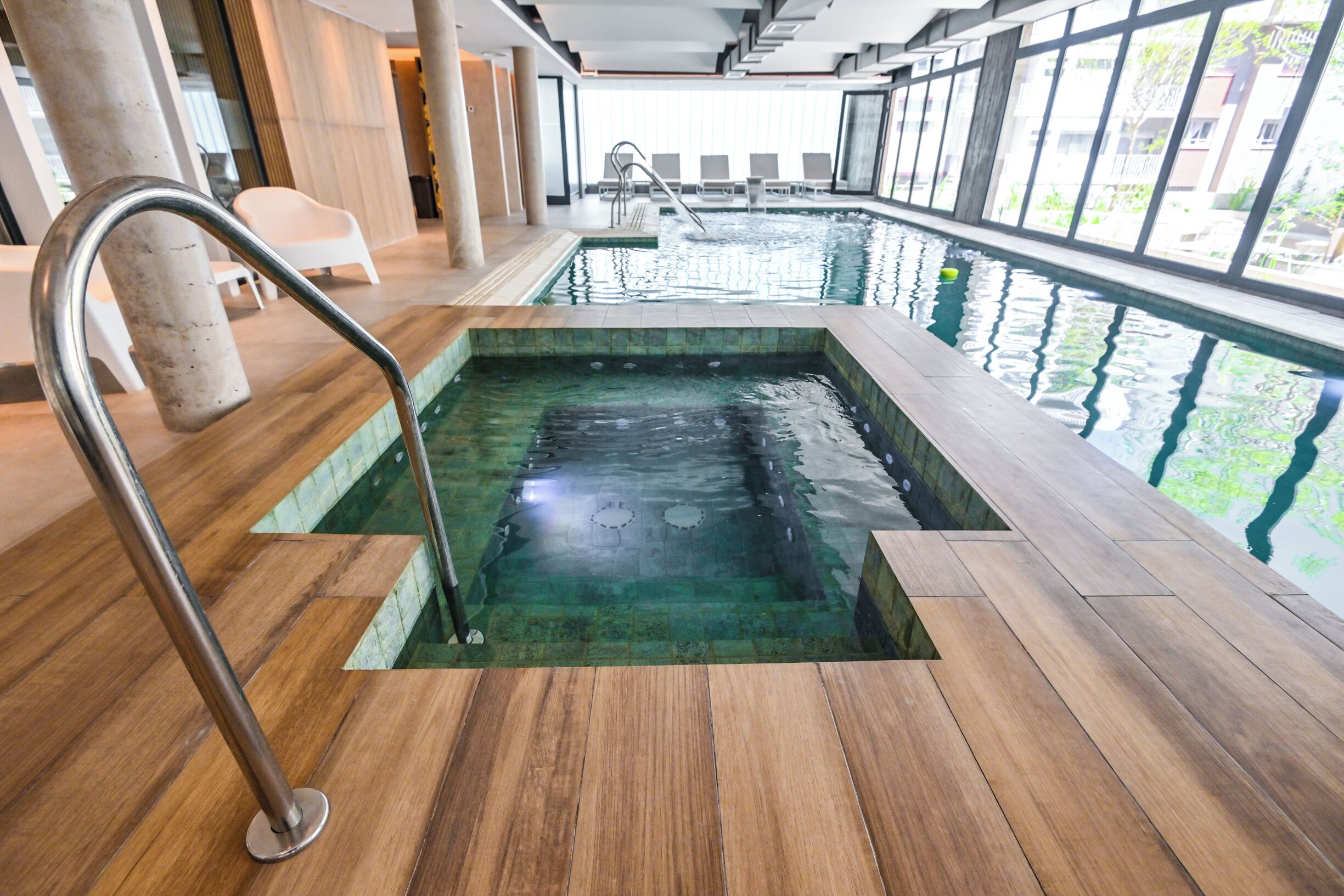 Una piscina interior con una terraza de madera y barandillas de metal.