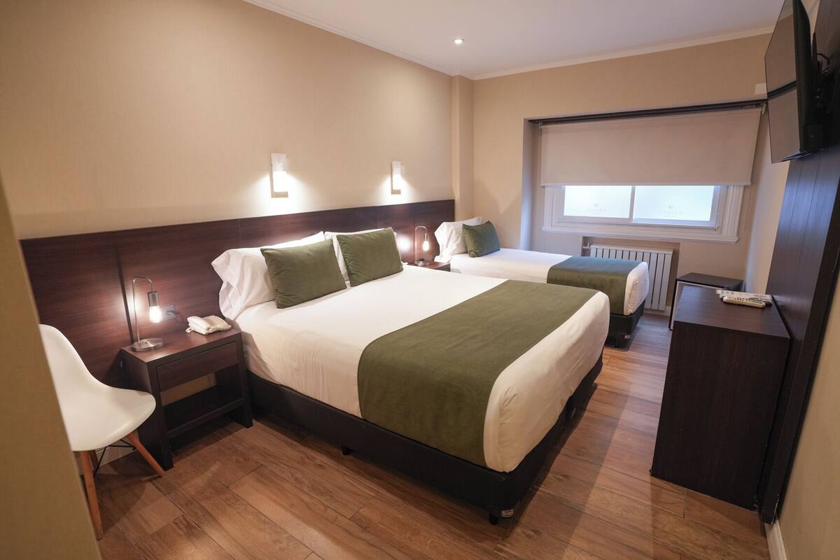 A hotel room with two beds, a desk, a chair, a TV, and a window with a view.