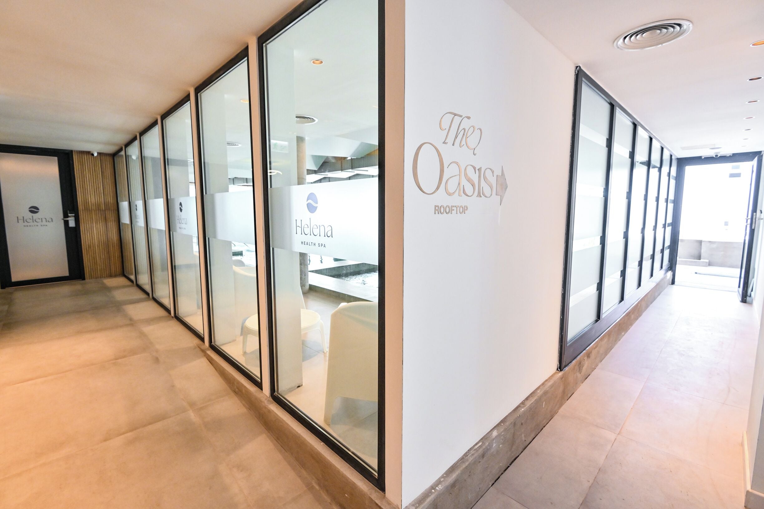 A hallway with glass doors and windows, leading to a spa area with a sign reading 'The Oasis Rooftop'.