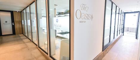 Un pasillo con puertas y ventanas de vidrio que conduce a un área de spa con un cartel que dice 'The Oasis Rooftop'.