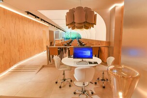 A modern conference room with a curved seating arrangement, a central table with a computer, and a unique ceiling light fixture.