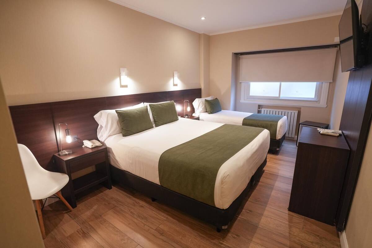 A hotel room with two beds, a desk, a chair, a TV, and a window with a view.