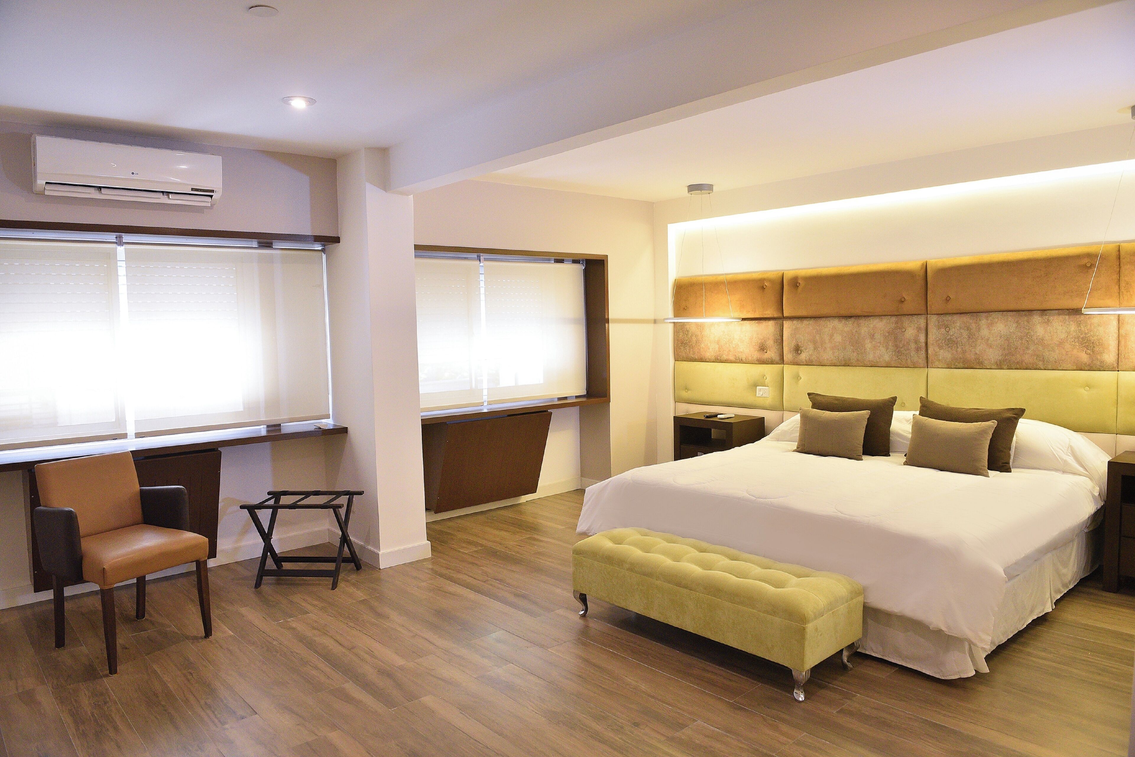 A modern hotel room with a large bed, a desk, a chair, and a window with blinds.