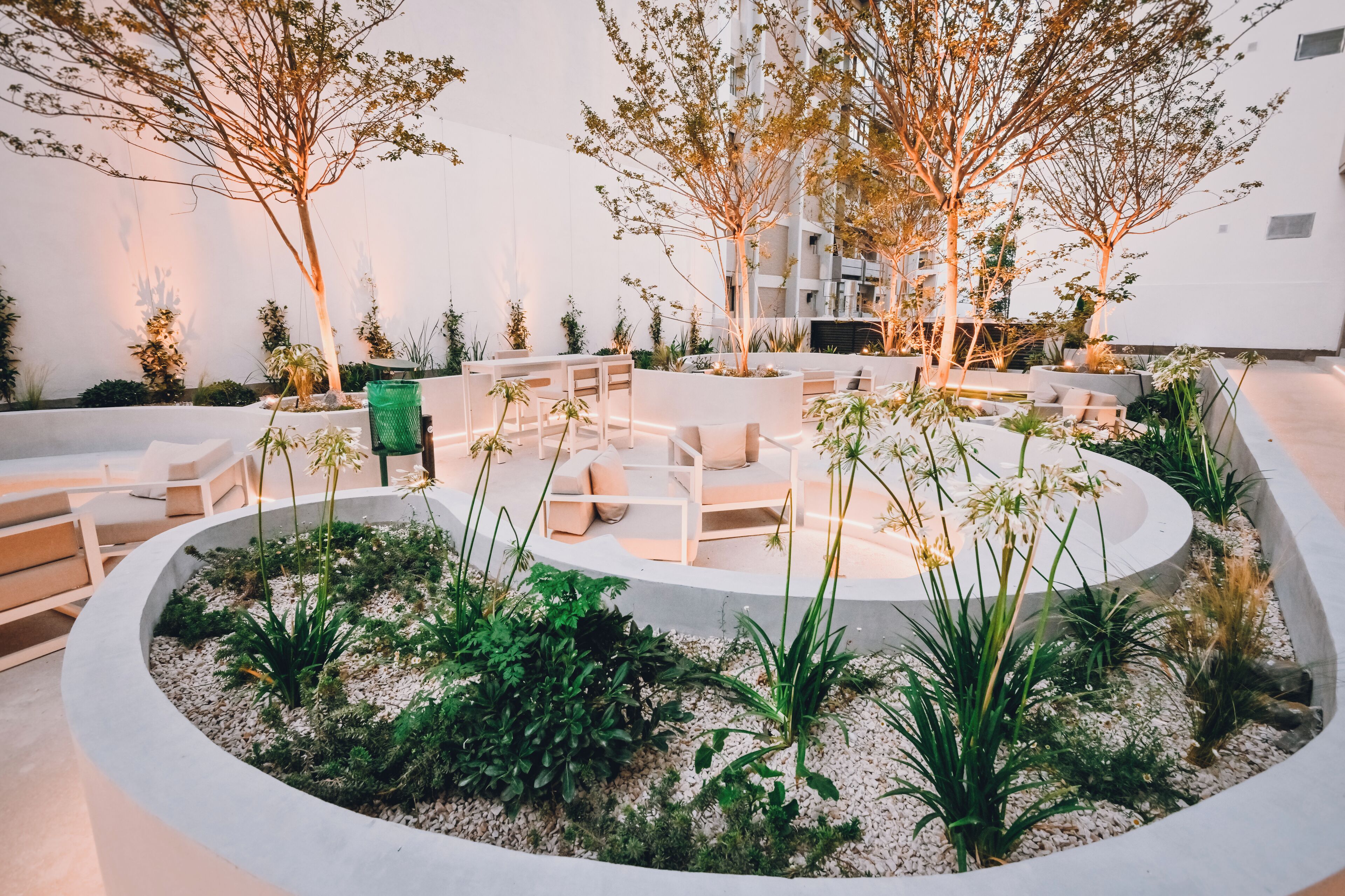 A modern outdoor seating area with white furniture and plants, surrounded by a circular concrete structure.