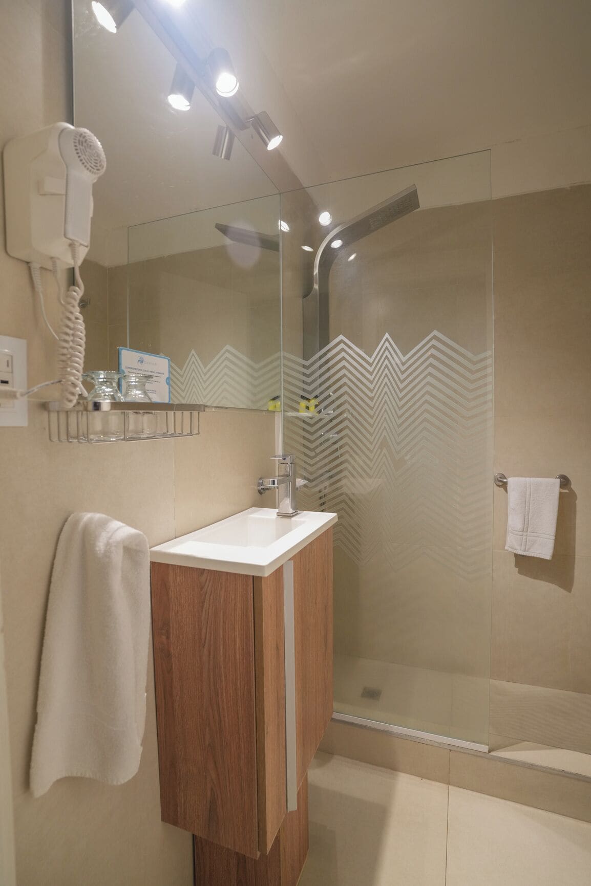 Un baño con tocador de madera, cabina de ducha de vidrio y espejo sobre el lavabo.