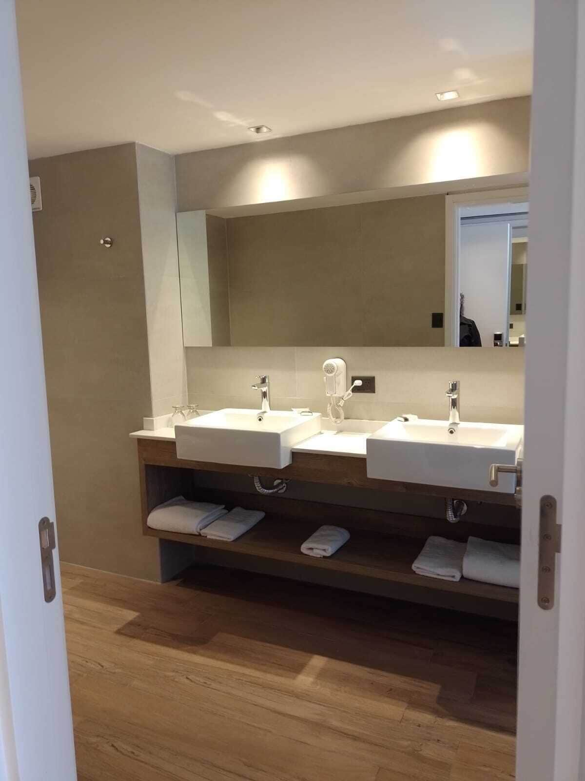 A modern bathroom with two sinks, a large mirror, and wooden flooring.