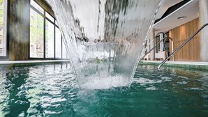 A modern indoor pool with clear water, a visible waterfall feature, and a staircase leading to an upper level. - Hotel Denver (Mar del Plata)