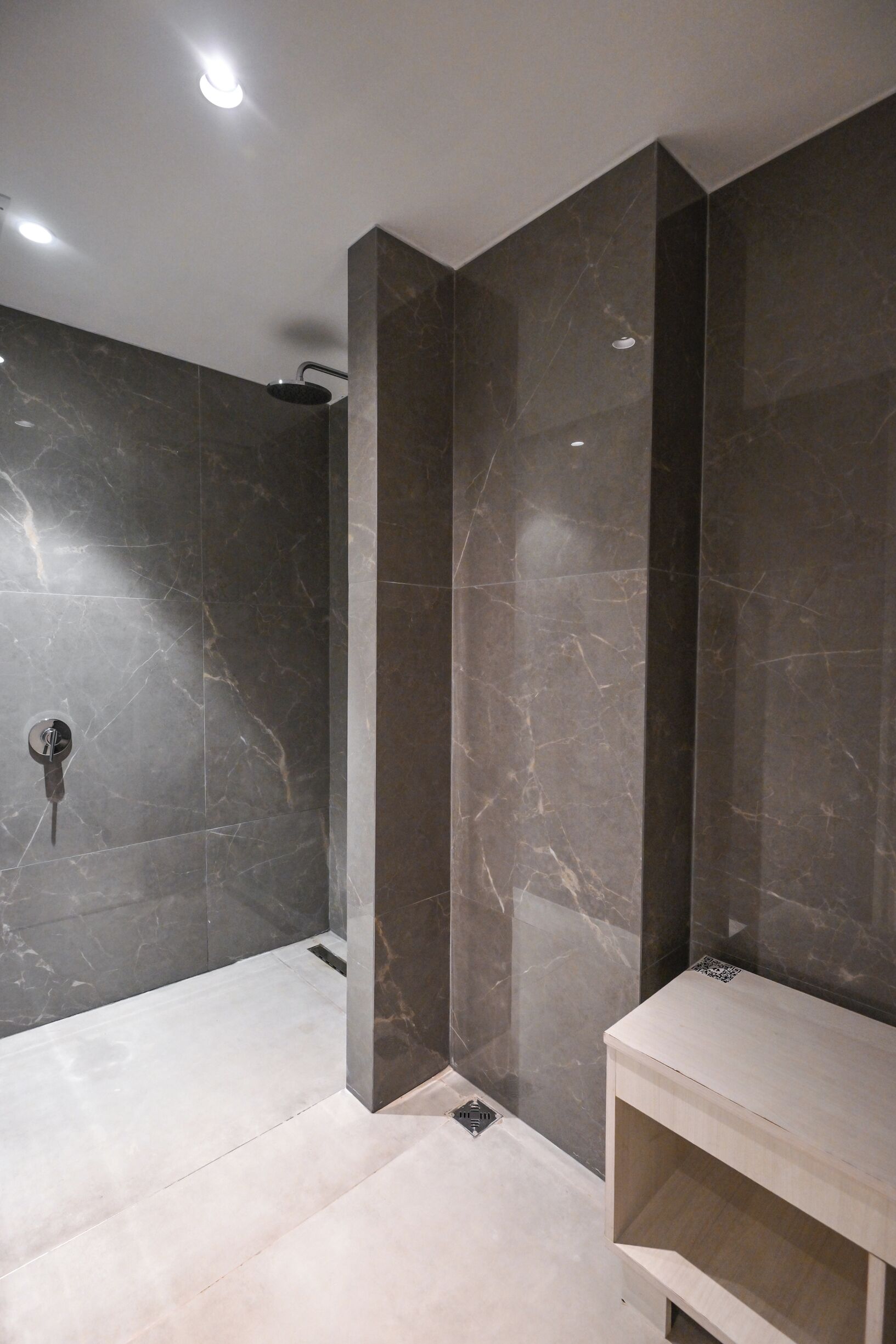 Un baño moderno con paredes de mármol oscuro, zona de ducha y tocador de colores claros.