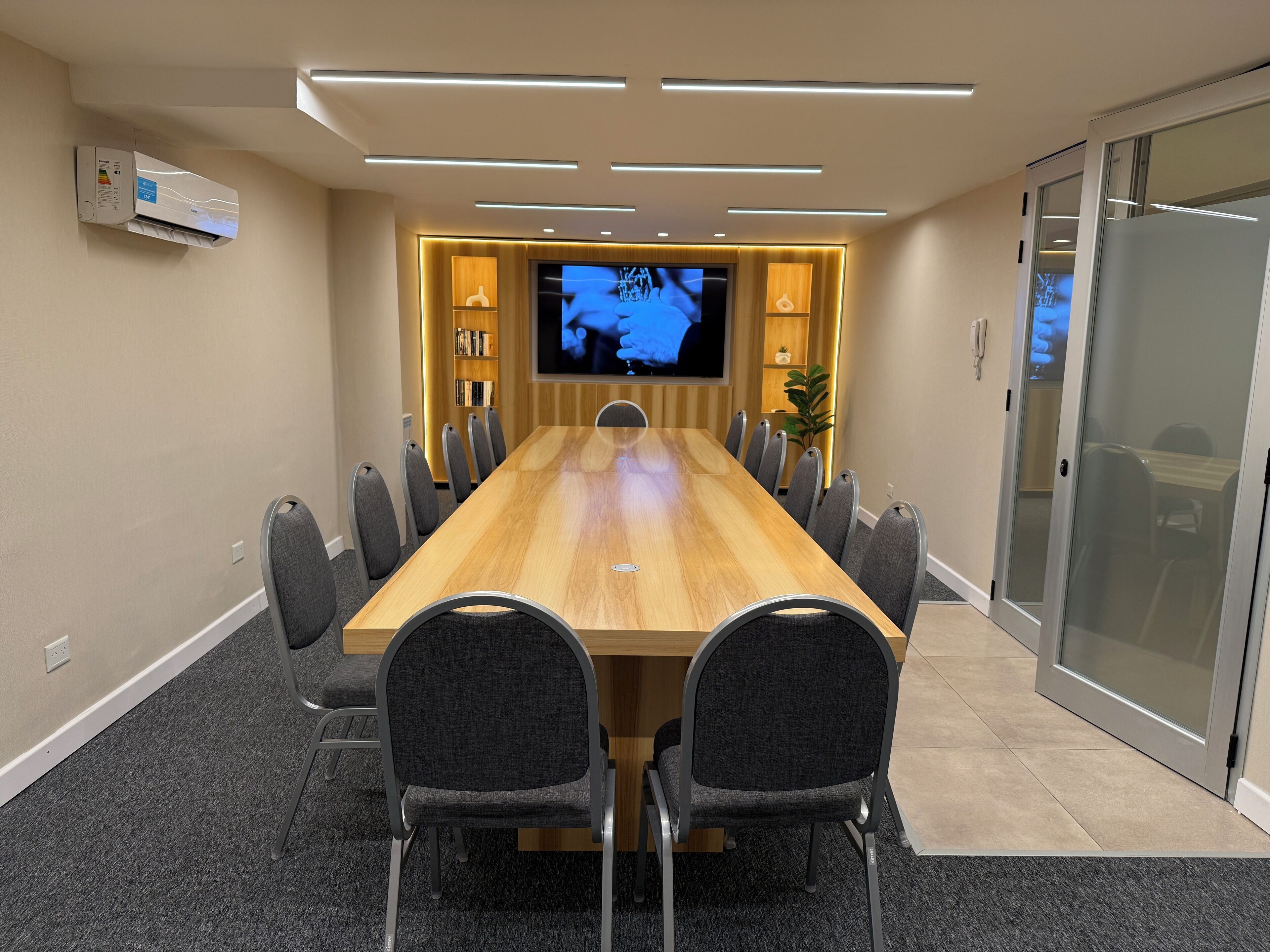 A conference room with a long table, chairs, a TV screen, and an air conditioning unit.