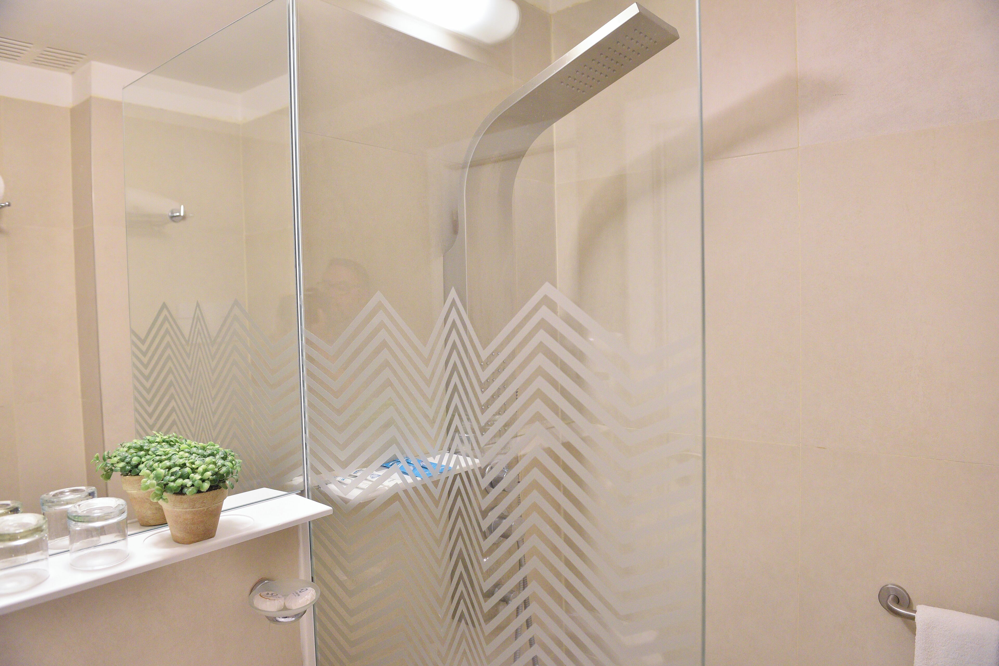 Een moderne badkamer met een douchecabine van glas, een spiegel, een plank met toiletartikelen en een decoratief behang.