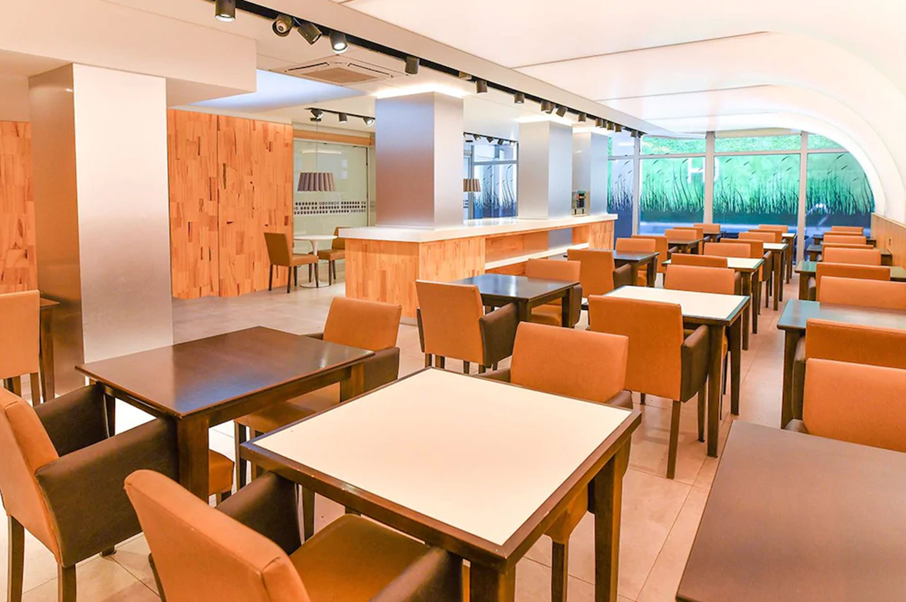 Un restaurante moderno con detalles de madera, una zona de bar y vistas a zonas verdes a través de grandes ventanales.