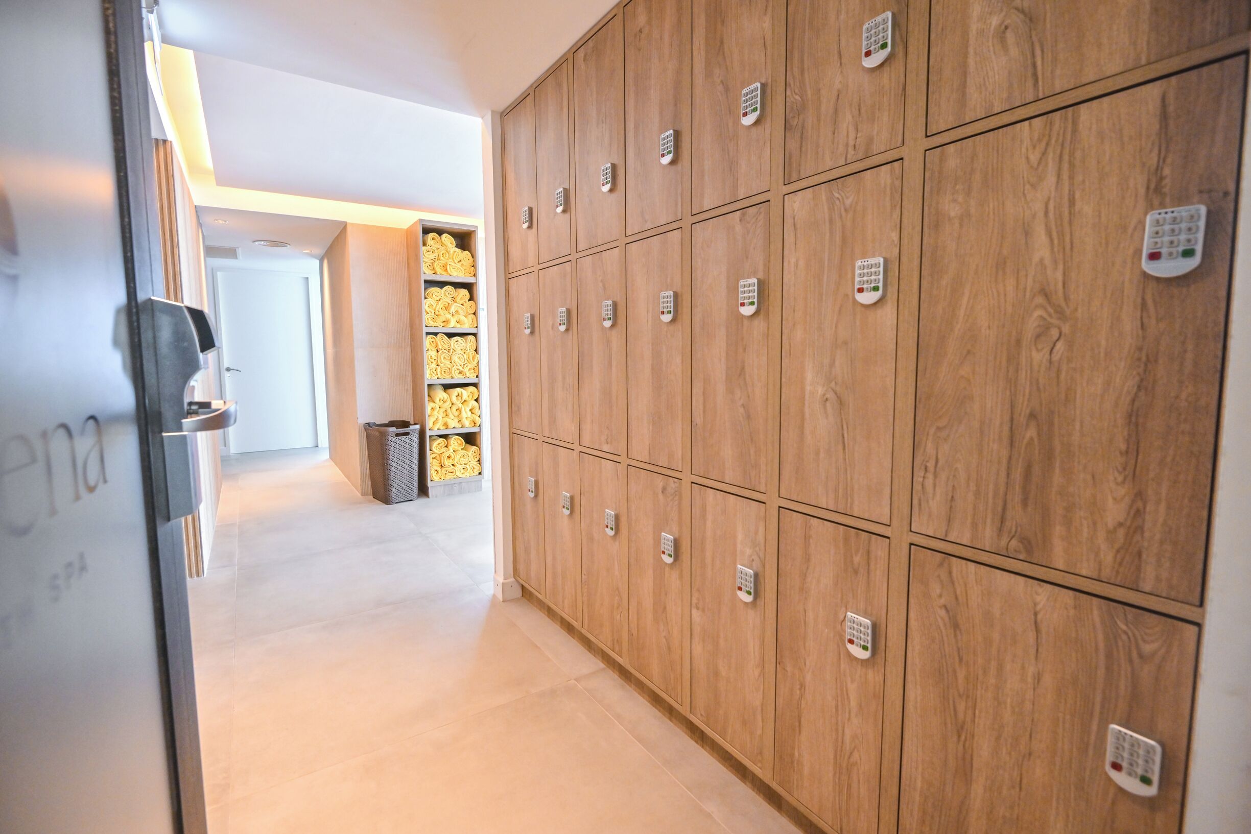 A hallway with a row of wooden lockers, a trash bin, and a door with a sign.