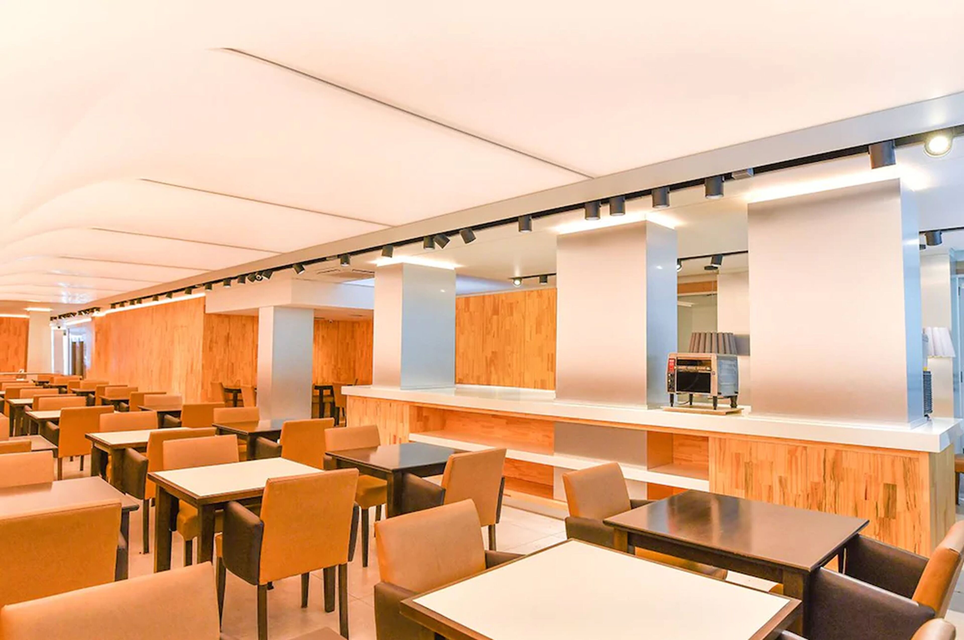 A modern dining area with multiple tables and chairs, wooden accents, and a counter with a coffee machine.