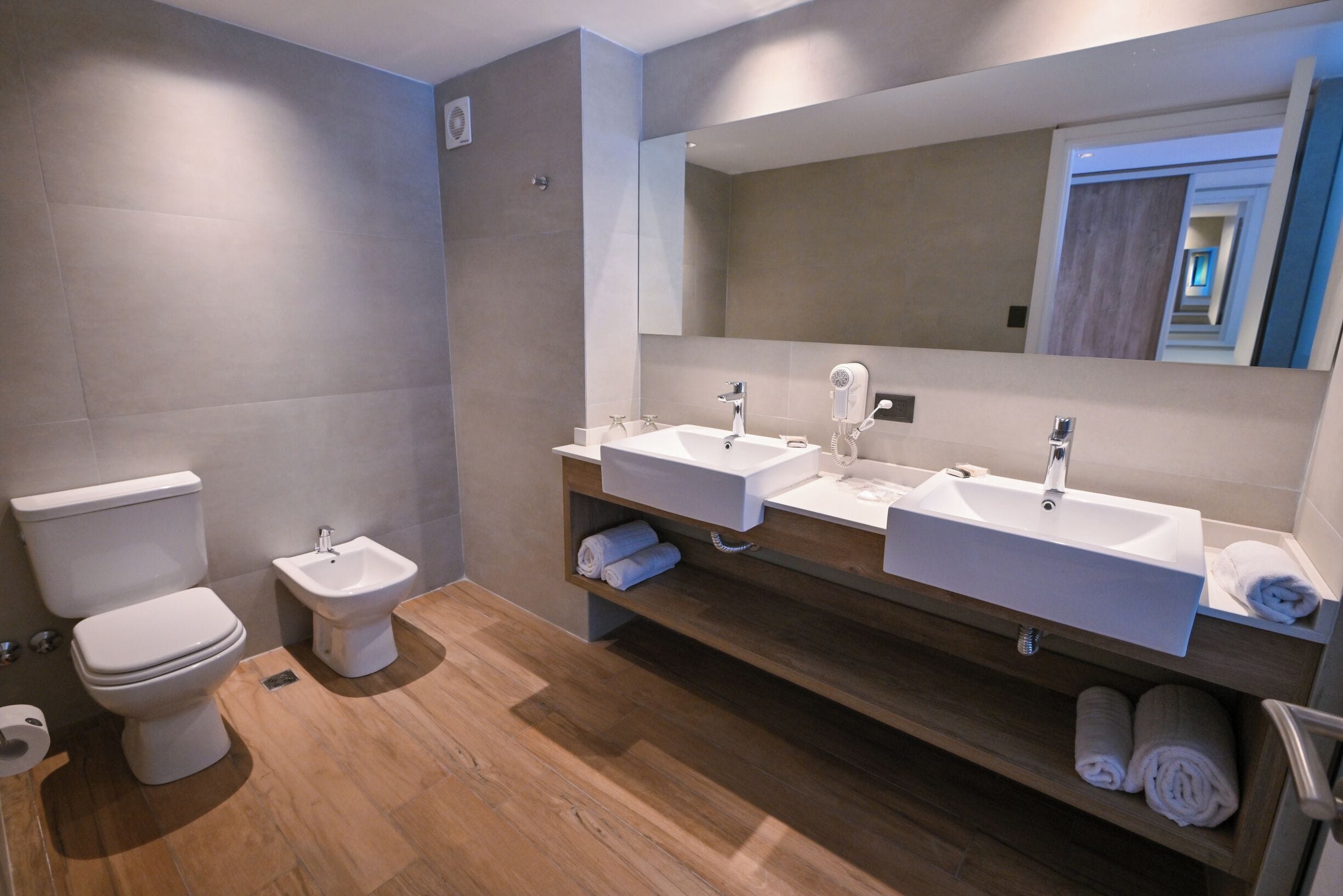 A modern bathroom with a toilet, bidet, and two sinks with mirrors.