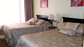 A hotel room with two beds, a nightstand with lamps, and a floral painting on the wall.