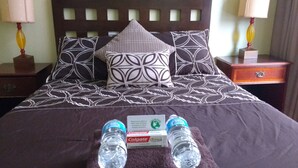 A neatly made bed with patterned bedding, two bottles of water, and a box of Colgate toothpaste on the bed. - Adelaide Hostel (San Francisco)