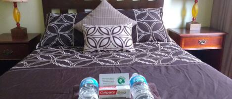 A neatly made bed with patterned bedding, two bottles of water, and a box of Colgate toothpaste on the bed.