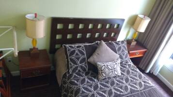 A hotel room with a bed, two bedside tables, a nightstand, a lamp, and a window with curtains.