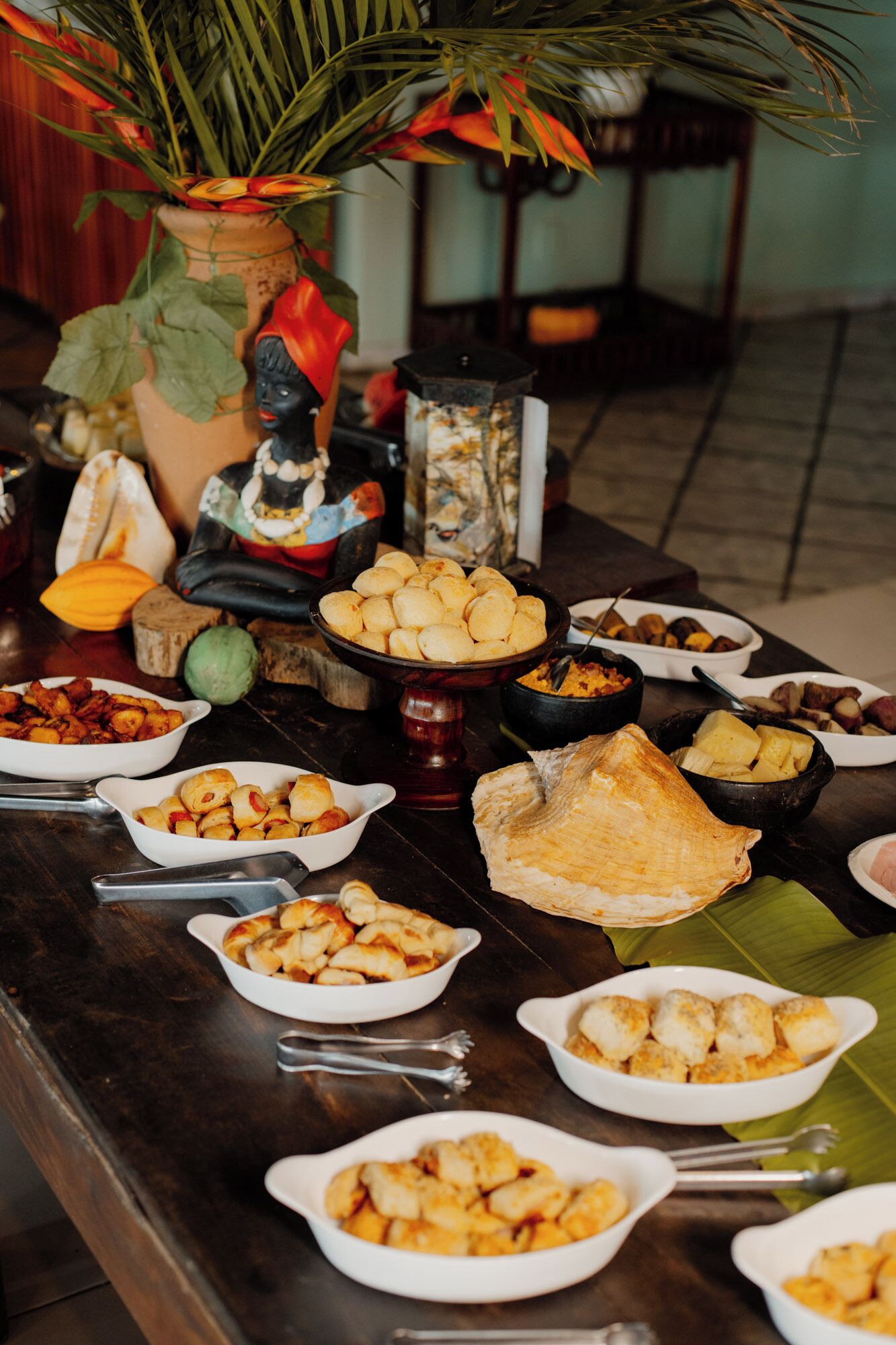 Een tafel met diverse gerechten, waaronder gefrituurde snacks en een groot stuk brood, geplaatst op een houten tafel met een decoratieve plant op de achtergrond.