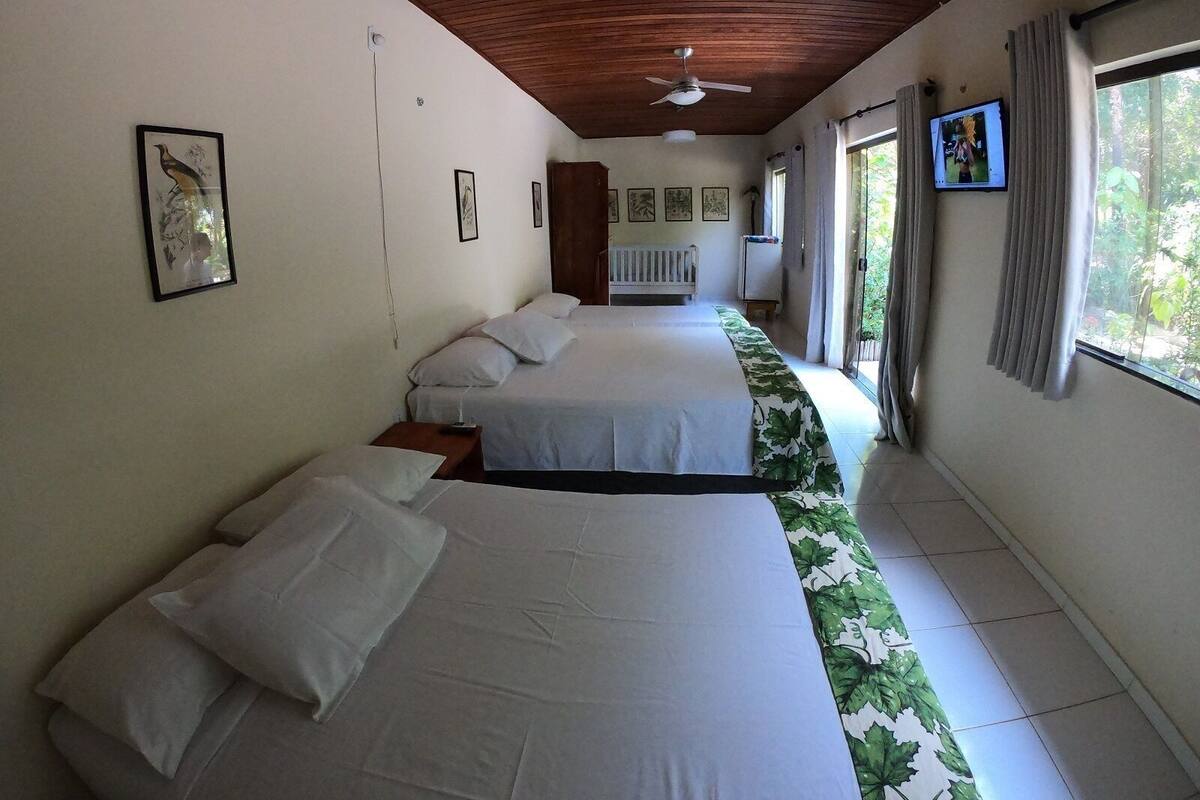 A hotel room with two beds, a ceiling fan, a television, and a window with curtains.