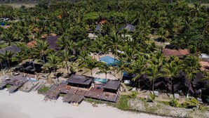 Een kustresort met diverse bungalowachtige accommodaties, een centraal zwembad en een strandgedeelte met ligbedden.