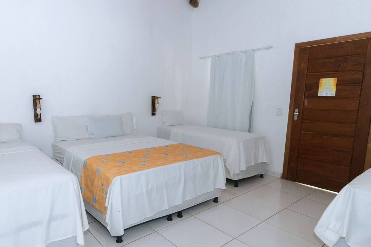 A room with three single beds, a wooden door, and a white tiled floor.